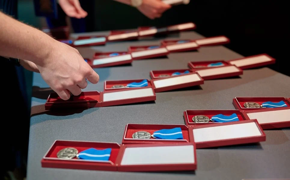 Kilkanaście Medali Stulecia Odzyskanej Niepodległości w czerwonych otwartych pudełeczkach
