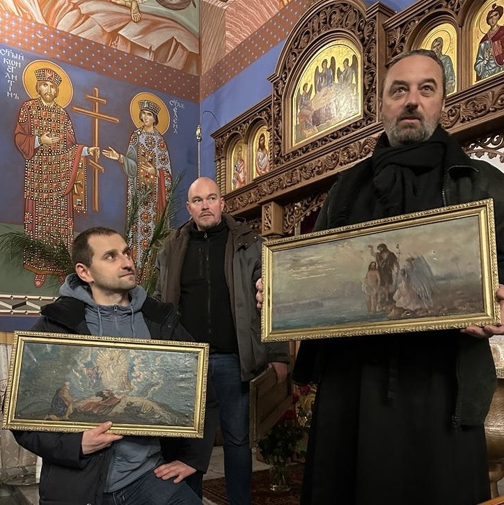 Mężczyźni trzymający obrazy religijne, z tyłu ściany budynku z licznymi malowidłami