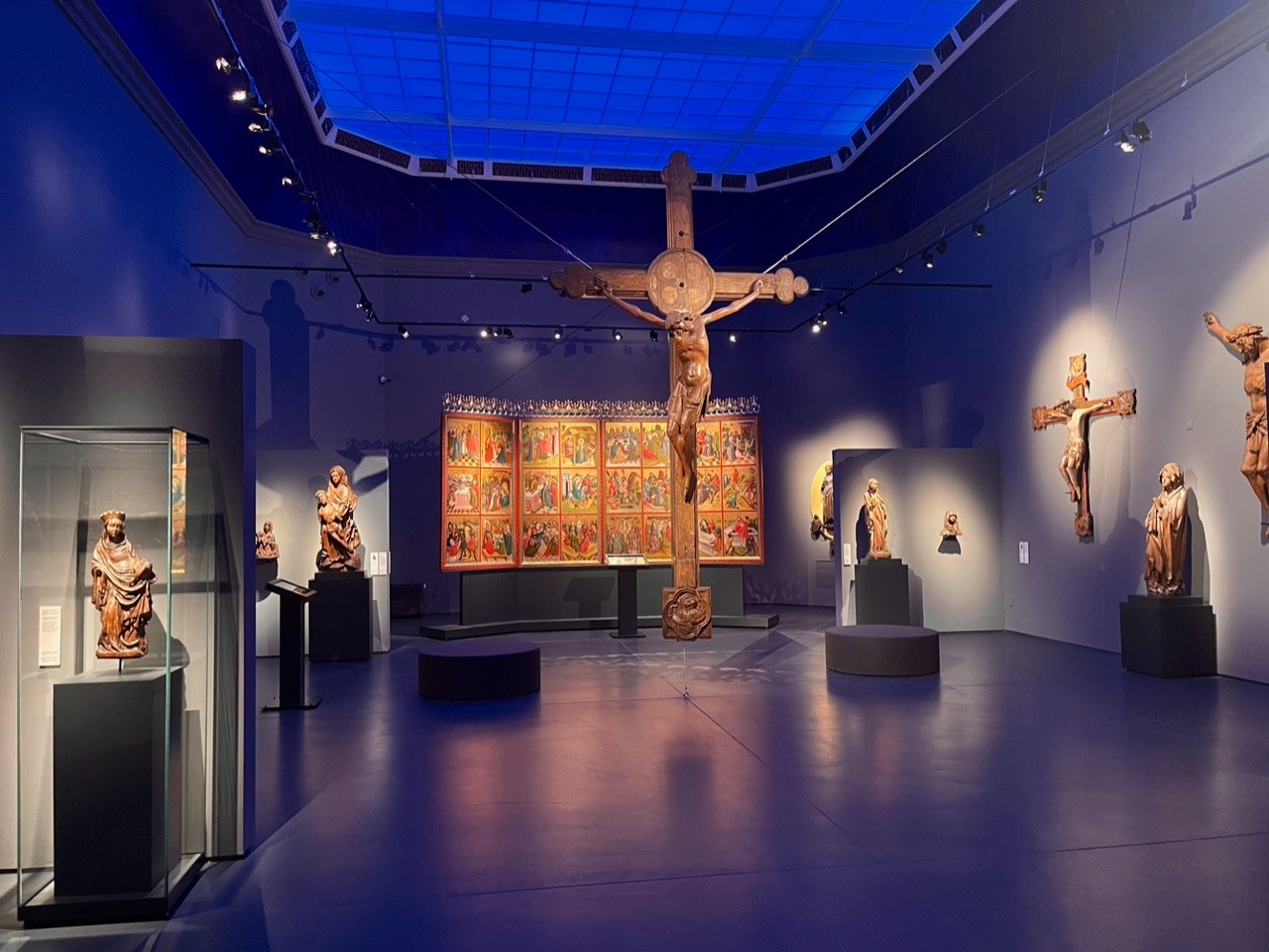 Pomieszczenie z dużym podwieszonym do sufitu krzyżem, na ścianach i w gablotach figury religijne